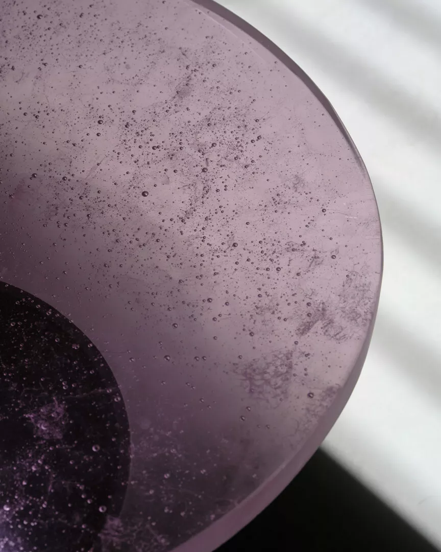 Close-up of textured purple glass disc with light shadows.