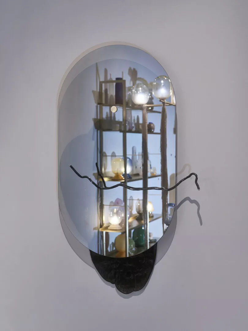 Reflective oval mirror displaying a shelf with various objects.