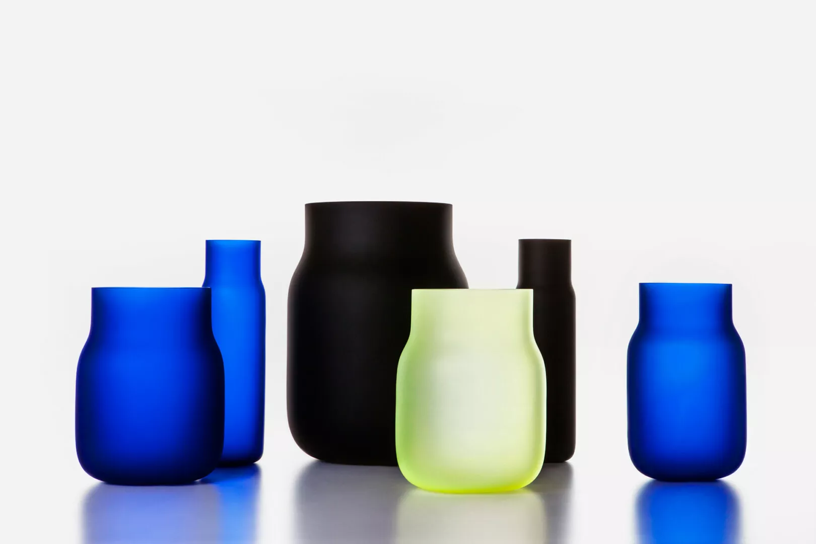Colorful modern vases on reflective white surface.