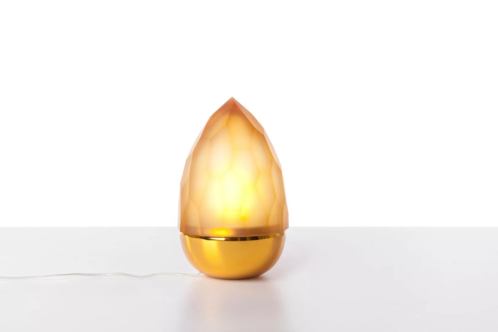 Illuminated amber teardrop-shaped lamp on white surface.