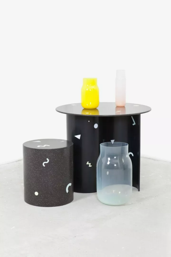Modern cylindrical tables with decorative vases on top.