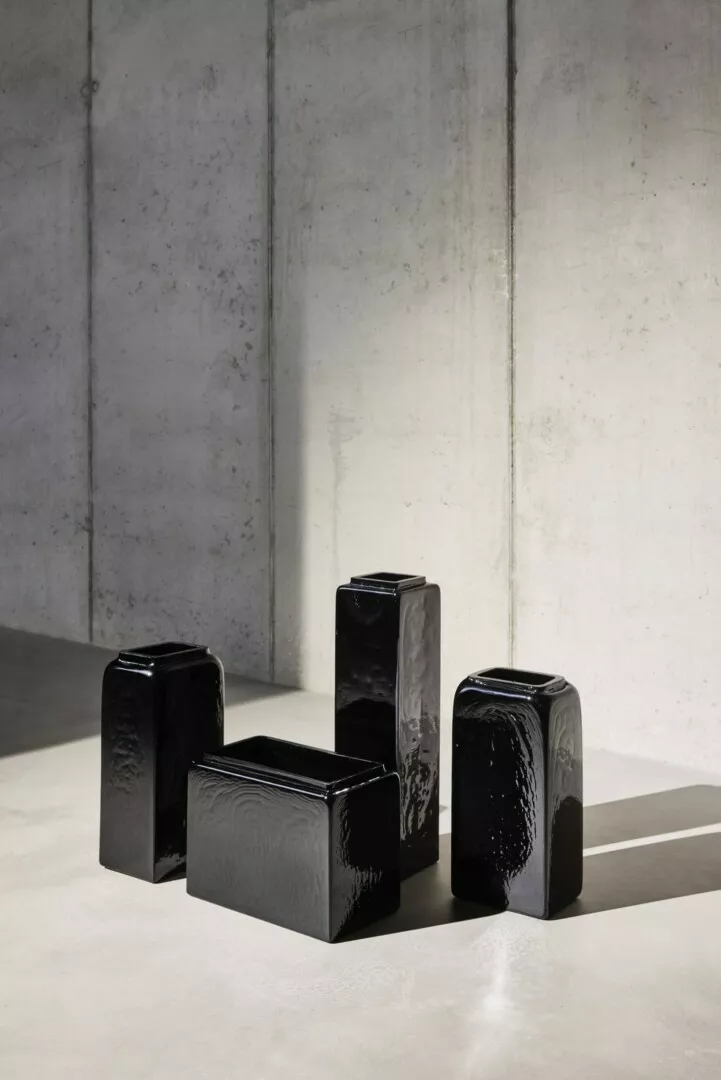 Five black ceramic vases on concrete floor.