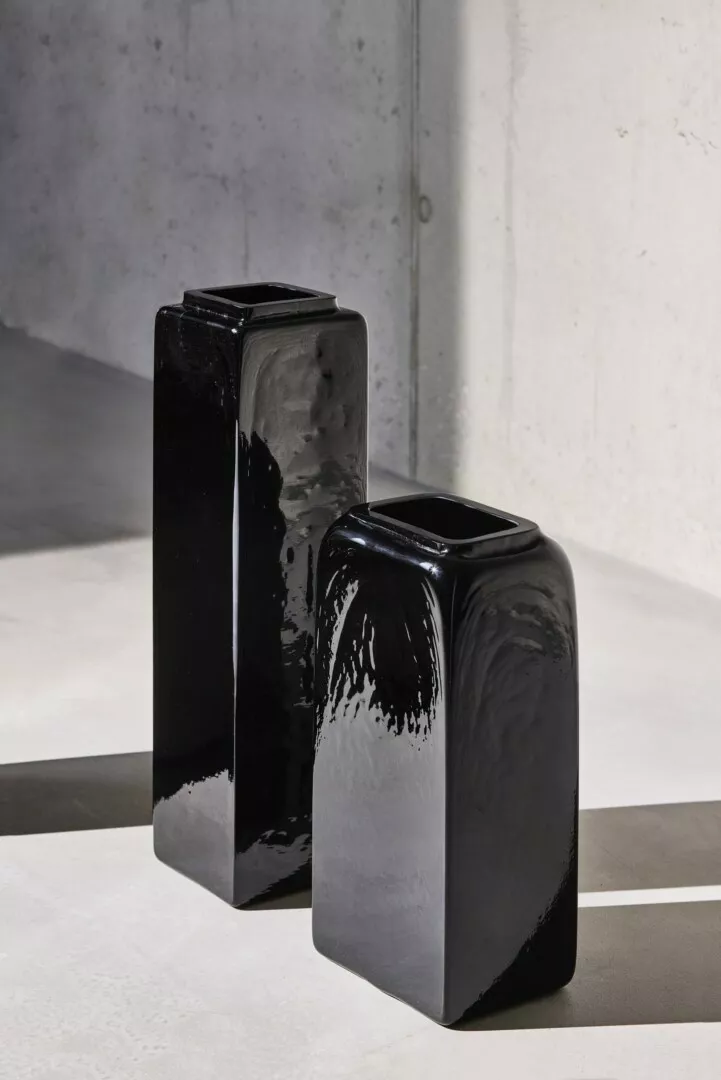 Two black ceramic vases on concrete floor.