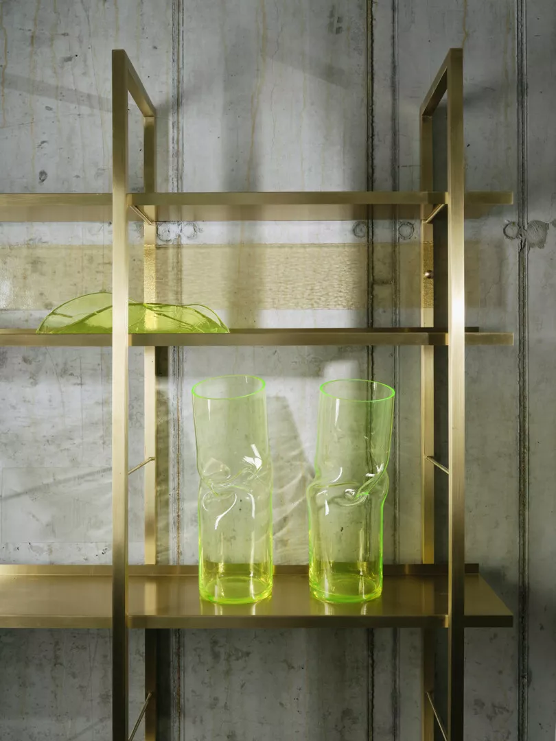 Modern gold shelf with green glass vases against concrete.