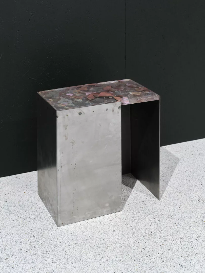 Modern metal side table with terrazzo top against dark wall.